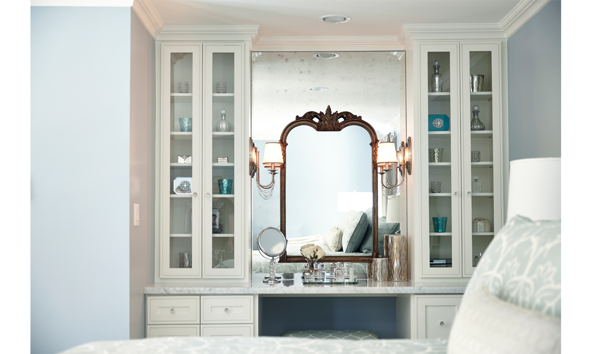 In a bedroom alcove, a spacious mirror and stylish dressing table with built-in vanity, glass cabinetry, and elegant lamp sconces create a refined ambiance.