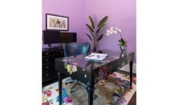 A cozy home office with a beautiful purple theme. A stunning black desk painted with bouquets, surrounded by lilac walls, artwork, and plants.