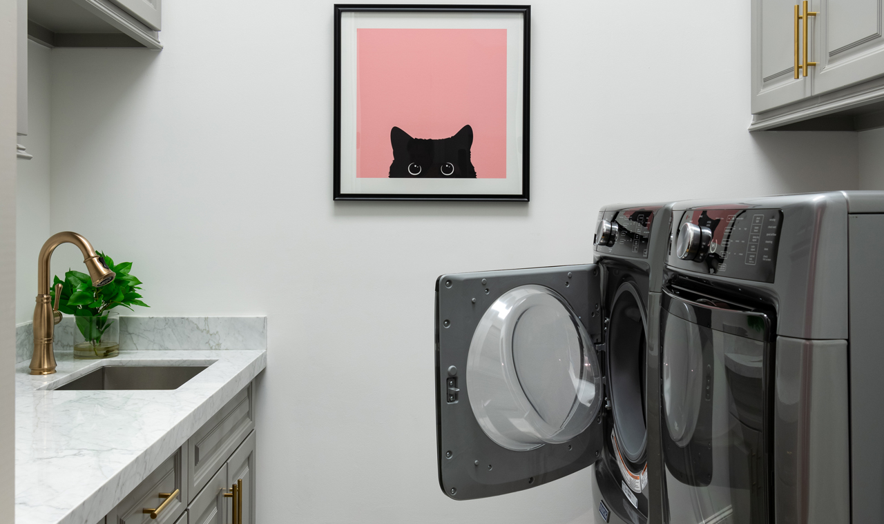 A cozy laundry room with a washer and dryer, cute cat art, and a utility sink with marble counters.