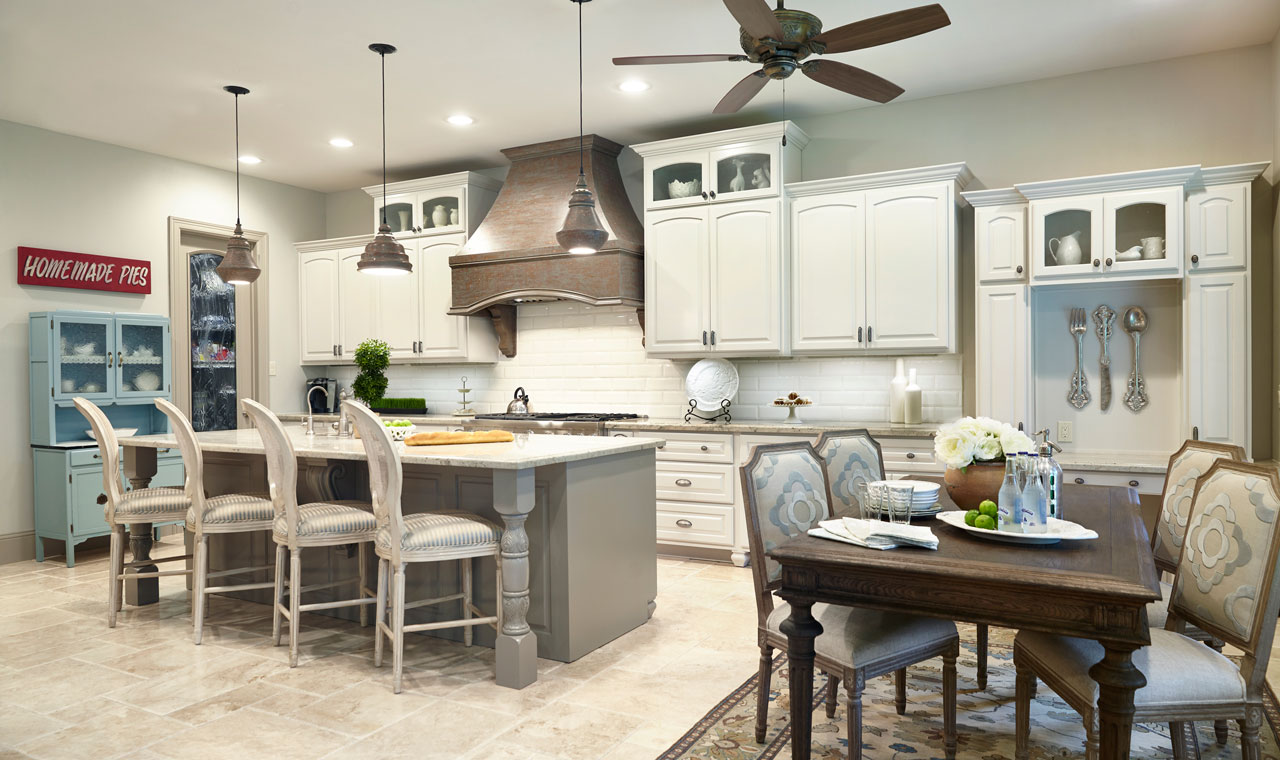 A charming kitchen blends rustic and Renaissance elements. White cabinetry, island with chairs, dining table, blue hutch, and a metallic stove hood.