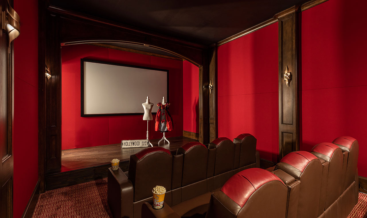 A cozy home theater with red walls, leather seats, popcorn, and stylish mid-century sconces.