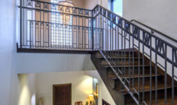 A renovated staircase with the original metal handrail, oak flooring, and a table. A chandelier above the front door adds elegance in the background.