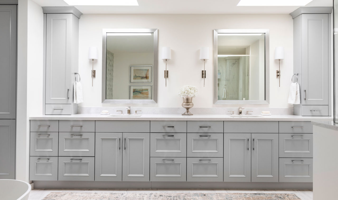 An elegant bathroom featuring ample gray cabinetry and matching mirrors, perfectly complemented by the lighting above the dual sink setup.
