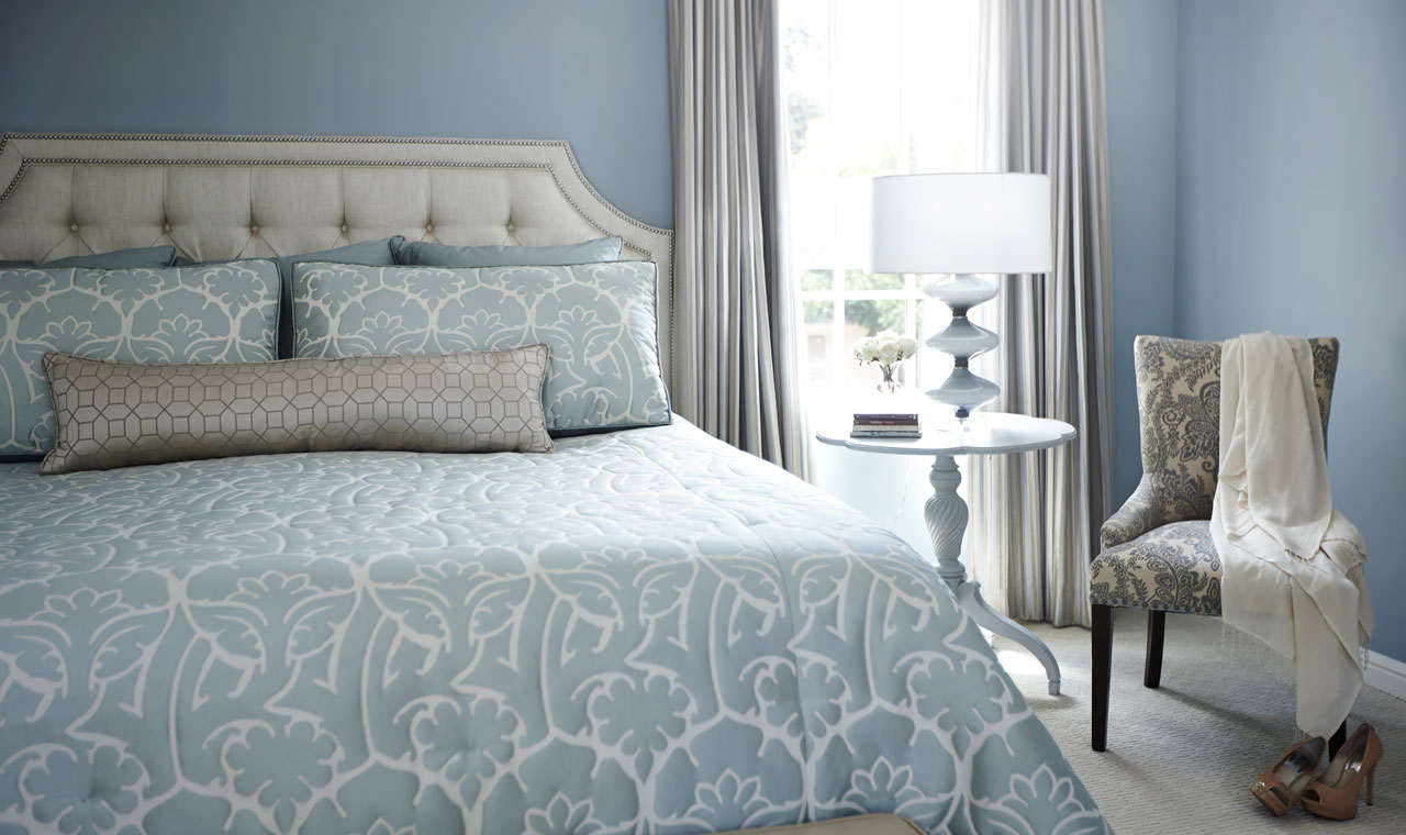 Serene blue-themed bedroom featuring a patterned comforter-clad bed against blue walls. Silver accents add a touch of sophistication to this peaceful sanctuary.