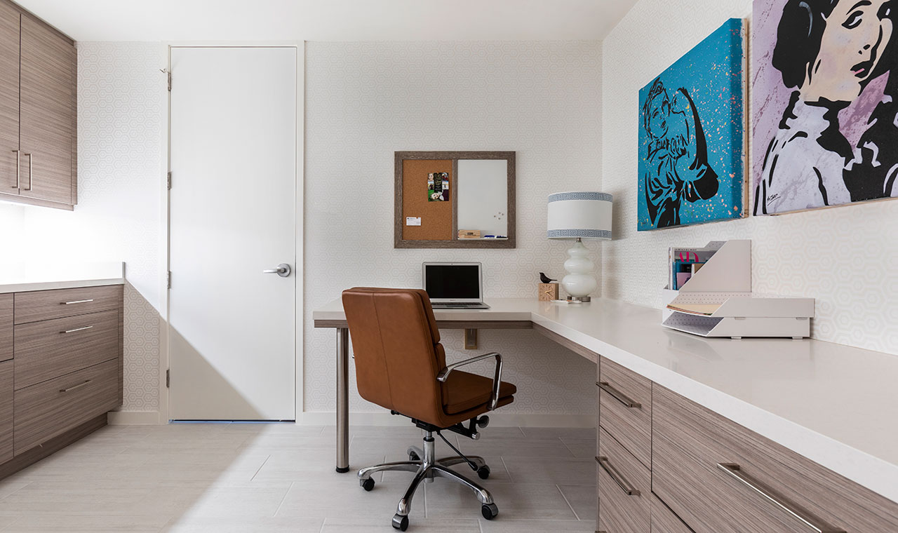 A cozy home office with a desk, chair, and vibrant art on the wall. Modern art deco brings color to this clean workspace.